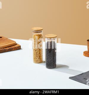 A Glass of food container with wooden lid, with utensils surrounding it, on a white and beige colored background. Stock Photo