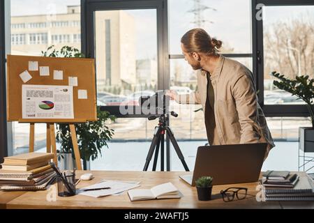 corporate manager adjusting digital camera on tripod near flip chart with graphs and office desk Stock Photo