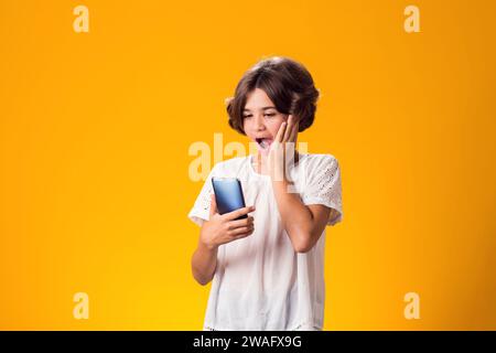 Surprised kid girl holding smartphone in hand over yellow background Stock Photo