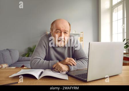 Portrait of senior man sitting with laptop computer at home and looking at the camera. Stock Photo