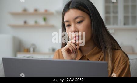 Smart pensive Asian chinese woman 30s businesswoman work from home kitchen thoughtful writer think business plan contemplate search media online on Stock Photo