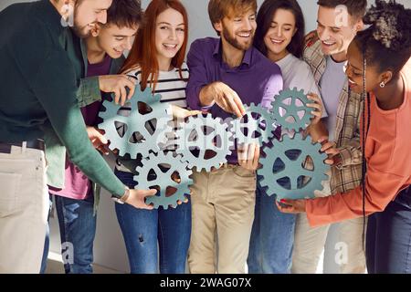 Group of happy smiling friends or business people connecting gears together. Stock Photo