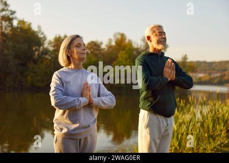 Active senior couple doing yoga exercises in nature. Outdoors fitness concept. Stock Photo