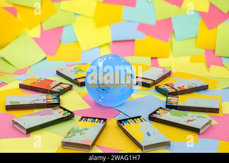 a crystal earth globe with 2024 Happy New Year made from golden chain links surrounded by matchboxes with colored sticks on a background of multicolor Stock Photo