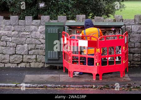 UK. A BT Openreach engineer working on wiring and cables in an open BT street cabinet. The engineer is wearing an Openreach reflective tabard Stock Photo