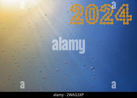 Soap bubbles in the blue sky with 2024 Happy New Year made from chain links. Beautifully iridescent balls of soap foam in the air with the rays of the Stock Photo