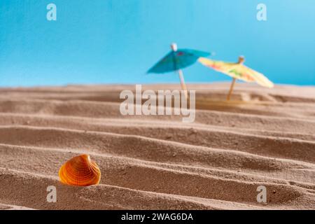 Seashells and cocktail umbrellas in the sand on a blue background, abstract texture for design, copyspace, summer concept Stock Photo