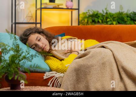 Tired 14-15 years child girl lying down in bed taking a rest at home. Carefree teenager female kid napping falling asleep on comfortable couch with pillows. Closed her eyes enjoy daytime nap alone Stock Photo