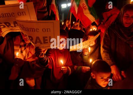 Kashmiri Shia Muslims hold placards and Iranian flags as they shout anti Israel and anti USA slogans during a candlelight vigil. In the outskirts of Srinagar, Kashmir, Shia Muslims from the Kashmiri community held a candlelight vigil expressing their opposition to Israel and the United States. The solemn gathering took a tragic turn as 84 individuals lost their lives, and numerous others sustained injuries in a blast during a ceremony commemorating the death of Iranian General Qassem Soleimani. The Islamic State claimed responsibility for the two destructive explosions that resulted in the dea Stock Photo