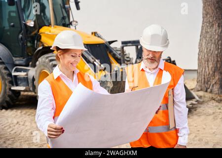 Team of construction specialists reading blueprints on development site Stock Photo