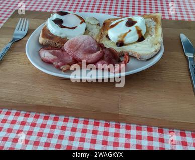 Breakfast on a plate. Poached eggs, toast, bacon and some brown sauce, on a plate, using a cutting board as a tray. Stock Photo