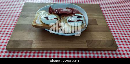 Breakfast on a plate. Poached eggs, toast, bacon and some brown sauce, on a plate, using a cutting board as a tray. Stock Photo