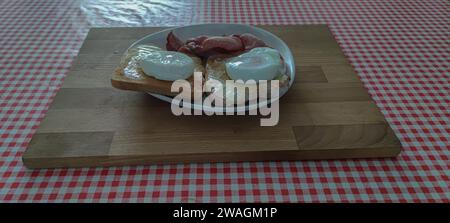 Breakfast on a plate. Poached eggs, toast and bacon, on a plate, using a cutting board as a tray. Stock Photo