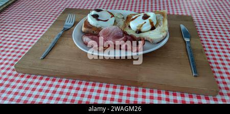 Breakfast on a plate. Poached eggs, toast, bacon and some brown sauce, on a plate, using a cutting board as a tray. Stock Photo