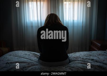 Woman sitting on the bed on her back with a depressive and tired attitude. Stock Photo