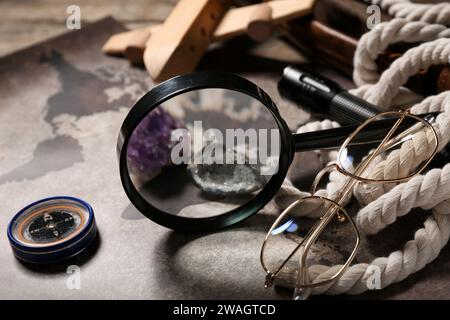 Magnifier with mineral stones, world map and travel equipment on brown wooden background Stock Photo