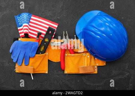 Belt with different tools, USA flag and hardhat on black grunge background. Labor Day celebration Stock Photo