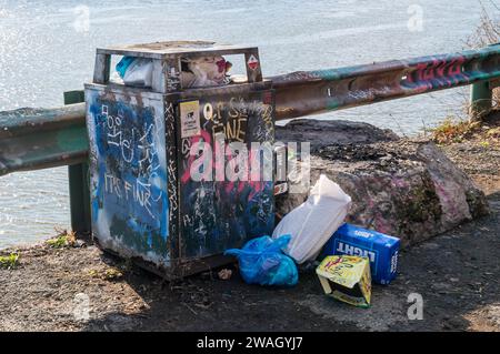 A graffiti covered overflowing garbage can on the banks of the Monongahela River in Pittsburgh, Pennsylvania, USA Stock Photo