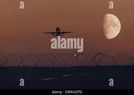 aircraft Airbus 320 climbing over runway in the evening twilight in front of a waxing crescent moon, Germany, Bavaria Stock Photo