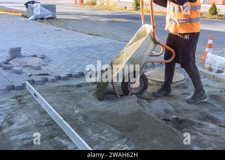 Pouring sand from wheelbarrow onto footpath in preparation for laying of decorative stones Stock Photo