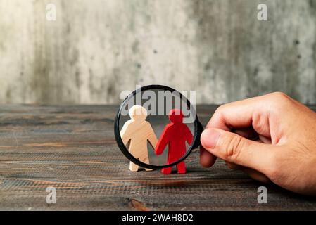 Magnifying glass focuses on a red wooden figure from the two wooden figures on a wooden table. Leadership concept Stock Photo