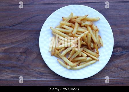 Salted French fries on white plate on a wooden table. Potato sticks. Junk fried unhealthy food concept. copy space. moody background. Stock Photo