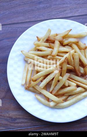 Salted French fries on white plate on a wooden table. Potato sticks. Junk fried unhealthy food concept. copy space. moody background. Stock Photo
