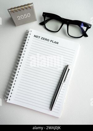Words "Net Zero Plan" on blank vertical notepad page with pen, empty space notebook with 2050 desk calendar. Climate neutral long term strategy sustai Stock Photo