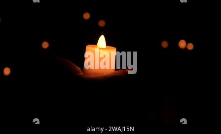holding a burning candle against a dark background Stock Photo