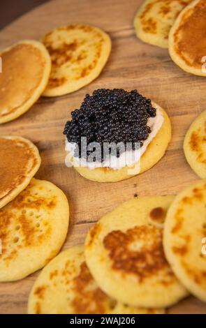 Blinis with black caviar and cream cheese, on a festive dish, mini pancakes, an elegant appetizer Stock Photo