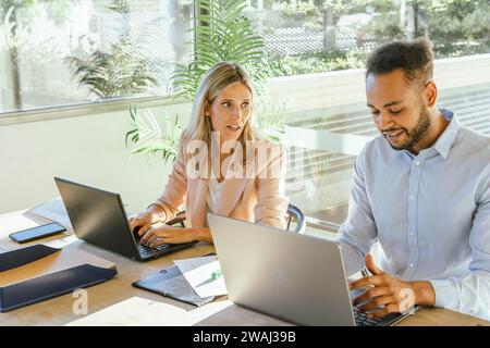 Two business co-workers talking while working with their computers at the office. Business concept. Stock Photo