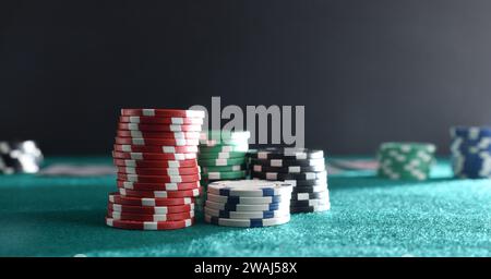 Detail of stacks of betting chips of different colors on green gaming mat with dark isolated background. Front view. Stock Photo