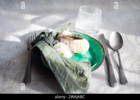 Closeup of Easter table setting, showcasing a vibrant green ceramic plate with two decorative Easter eggs adorned with white and green patterns and de Stock Photo