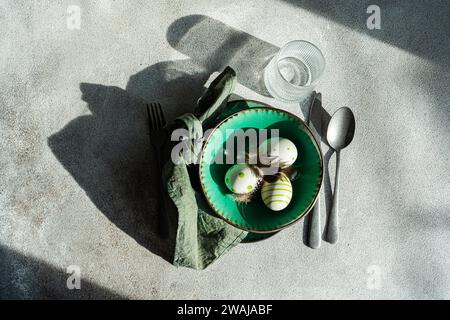 Top view of Easter table setting, showcasing a vibrant green ceramic plate with two decorative Easter eggs adorned with white and green patterns and d Stock Photo