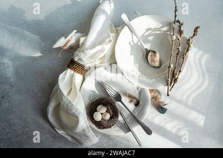 Top view of elegant Easter dining arrangement, featuring pristine white plates with a delicate embossed design with woven nest containing speckled egg Stock Photo