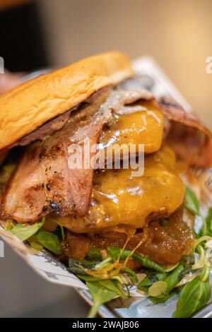 Gourmet beef burger with melted cheddar, crispy bacon, caramelized onions, and fresh greens on a brioche bun, served on a newspaper-lined plate Stock Photo