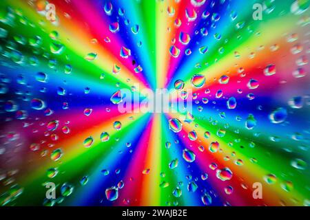 A radial burst of vibrant rainbow colors blurred behind a pattern of clear water droplets on a glass surface Stock Photo