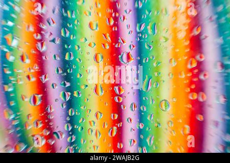 Water droplets on a glass surface with a blurred background showcasing a spectrum of colors in vertical lines Stock Photo