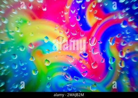 Glass surface with water droplets over a swirling, colorful abstract background with shades of the rainbow Stock Photo