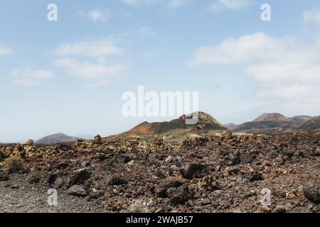 Jagged lava rocks spread across the foreground with gentle volcanic hills under a cloudy sky in the Lanzarote landscape Stock Photo