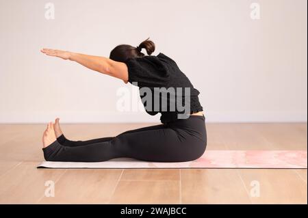 Full body of unrecognizable lady in activewear sitting on mat and practicing yoga during yoga class Stock Photo