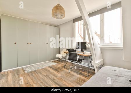 Computer on wooden work desk in spacious bedroom of modern apartment with chairs and window Stock Photo
