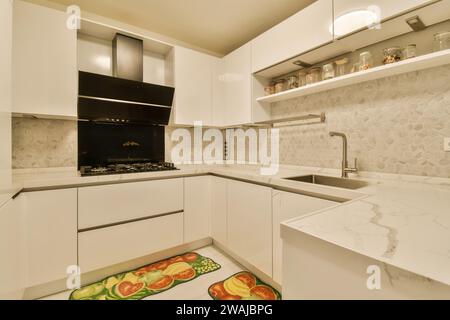 Rangehood over stove with sink at marble countertop with jars on shelf in illuminated modern white kitchen Stock Photo