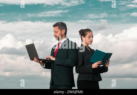Businessman and businesswomen. Beautiful young business woman and handsome businessman in formal suits are using a laptop standing outdoor. Stock Photo