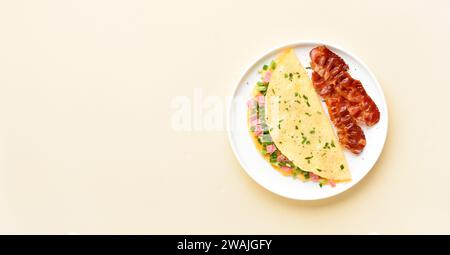 Stuffed omelette with ham, green onion and roasted bacon on plate over light background with copy space.  Top view, flat lay. Stock Photo