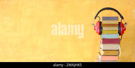 Relaxing with audiobooks concept with heap of books and vintage headphones.Bright yellow background with large copy space Stock Photo
