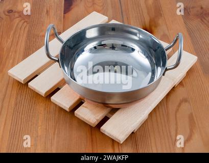 Traditional Classic hard wood hand made trivet  with a copper bottomed hot Balti Indian curry dish on a kitchen worktop Stock Photo