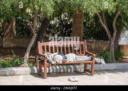 Valletta Malta Xlokk Malta September 07 2023 Poor homeless colored man sleeping on an open park wooden bench  with his shes off Stock Photo