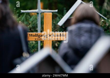 Offenburg, Germany. 05th Jan, 2024. Mourners stand in front of the wooden cross with the inscription 'Wolfgang Schäuble' at the cemetery after the funeral service for Wolfgang Schäuble (CDU). Credit: Uwe Anspach/dpa/Alamy Live News Stock Photo