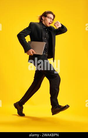 Young man, dressed smart casual outfit looks at his watch in surprise and realizes that he late for interview against yellow studio background. Stock Photo